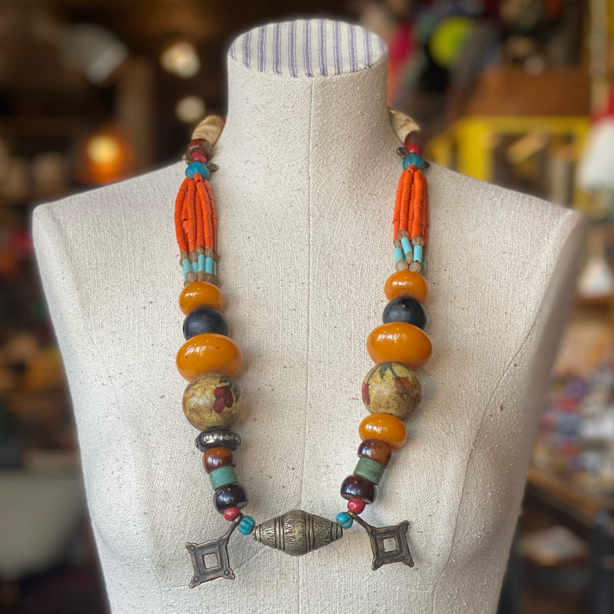 Bold and colorful statement necklace featuring large orange and turquoise beads, tribal-inspired charms, and intricate detailing, named Itahari.
