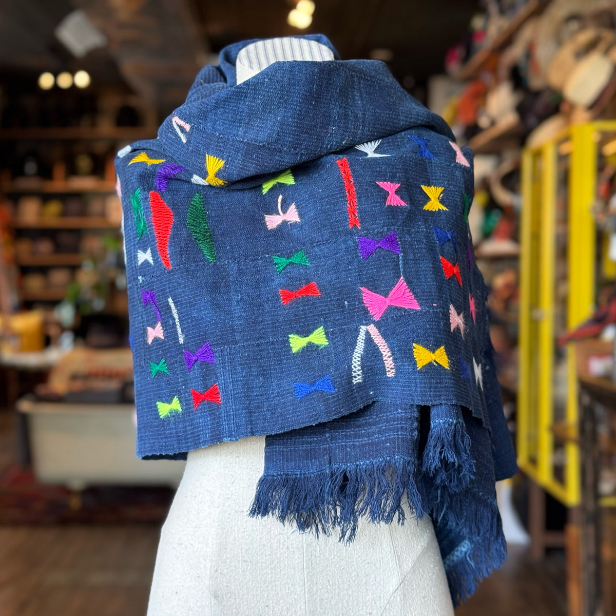 Vintage Indigo Mud Cloth Scarf No. 1 draped on a mannequin, featuring a deep indigo base with vibrant multicolored embroidered accents and fringed edges.