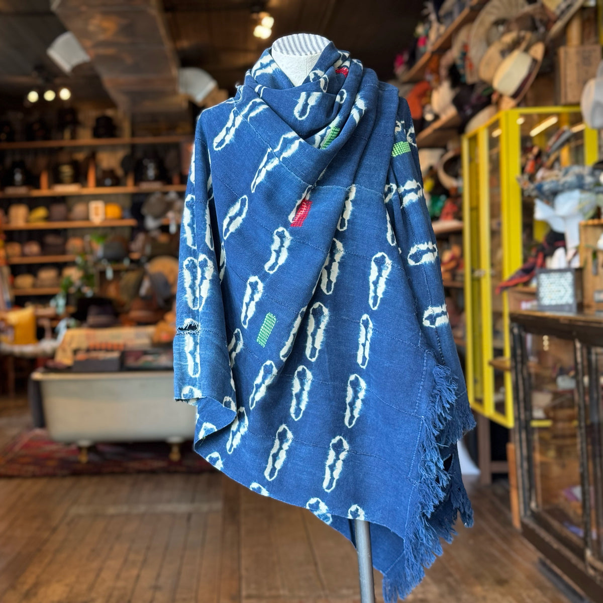 Blue patterned fabric with white and green designs draped on a mannequin in a vintage-style shop, showcasing the Vintage Indigo Mud Cloth Scarf No. 4.