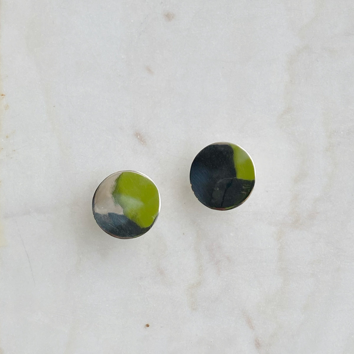 Sterling Disc Earring pair with smooth, polished round surfaces reflecting subtle shades of silver and dark tones on a light marble background.
