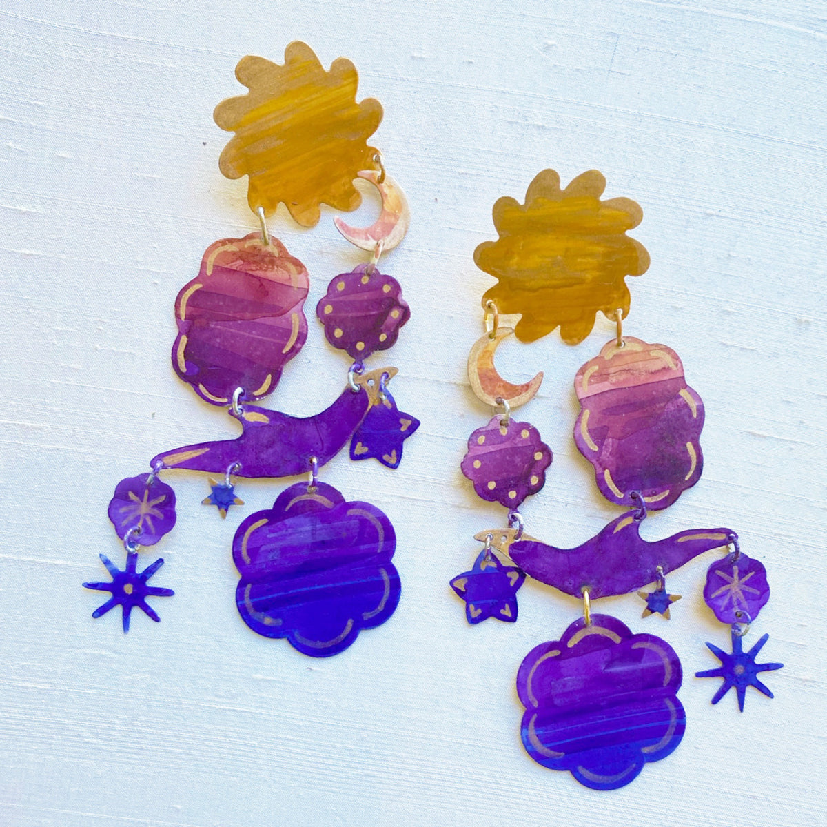 Gilded Sunset Earring featuring layered shapes in warm amber and purple hues with celestial-inspired star, moon, and cloud charms in a playful dangling design.