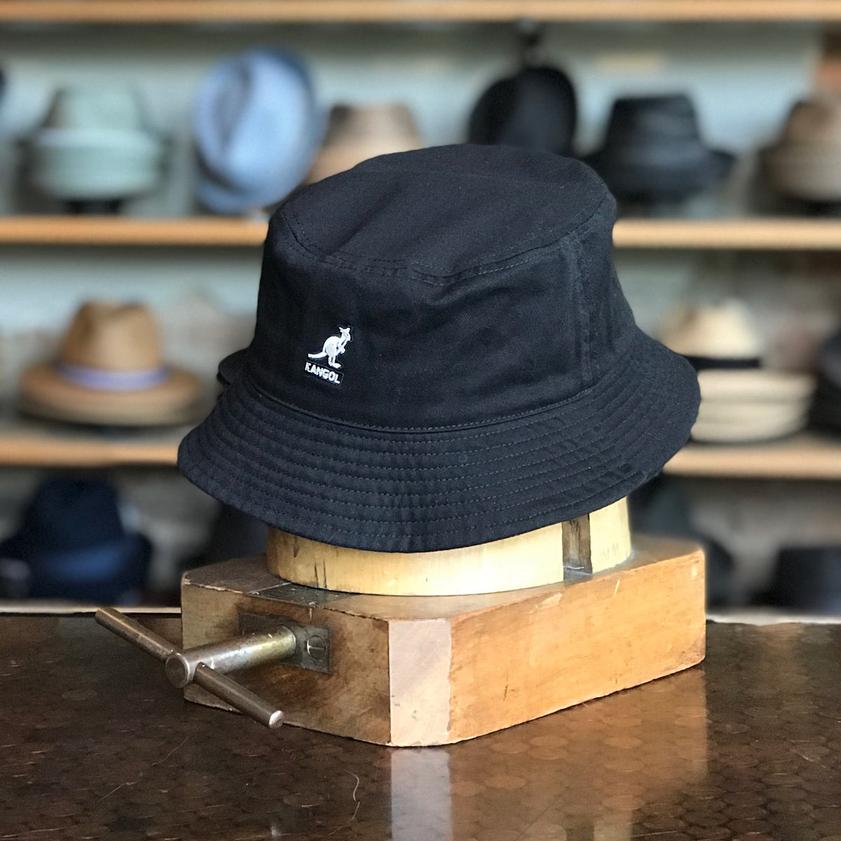 Black Washed Bucket Hat displayed on a wooden hat block, featuring a soft fabric build and a subtle logo detail, perfect for casual and stylish accessory use.