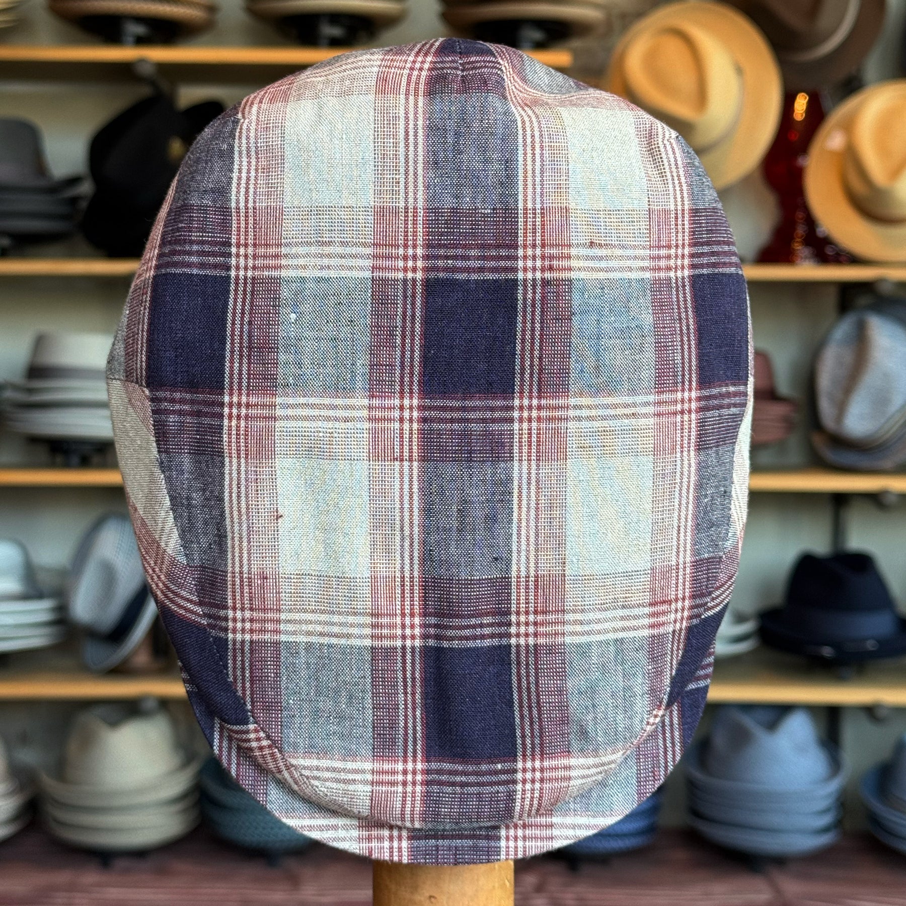 Americana Vintage Flat Cap featuring a classic plaid pattern in muted tones, displayed against a backdrop of various hats, highlighting its vintage charm and style.