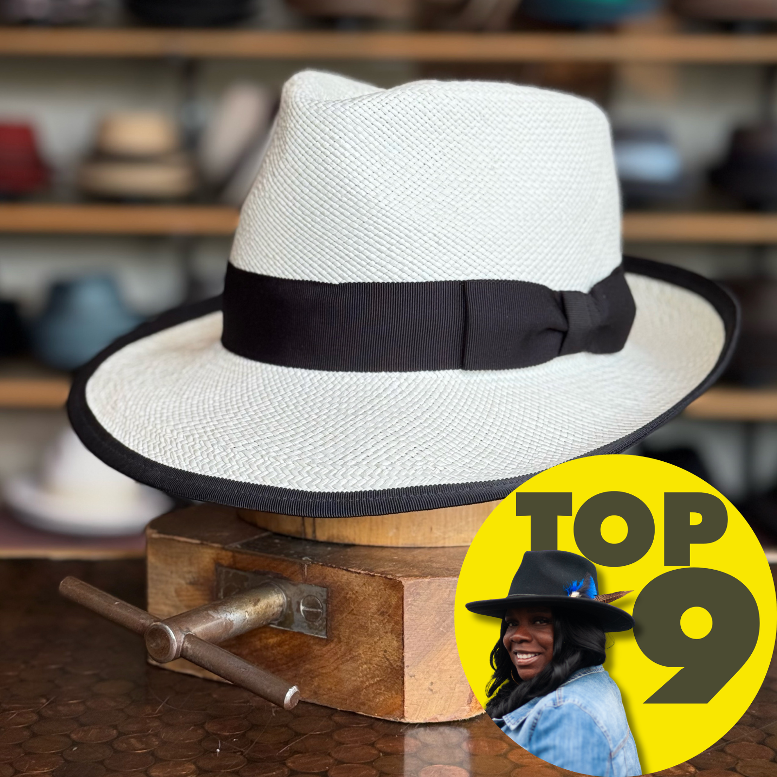 Clover Club white textured fedora hat with a black band and trim, displayed on a wooden stand in a store setting with various hats blurred in the background.