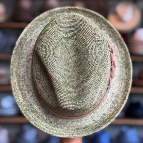 Top of Crochet Tino Fedora in green with a brown band, showcasing its textured material and classic fedora shape among other hats in the background.