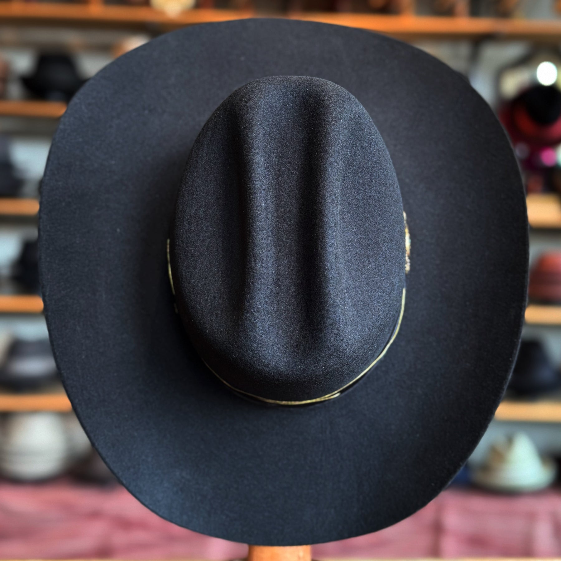 Black wide-brimmed felt hat with a distinct crease crown, displayed on a wooden stand in a hat shop, showcasing the Daredevil style.