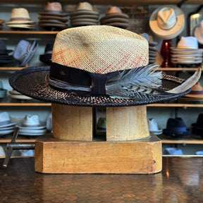 Dark Star Mel Fedora featuring a two-tone woven design with a natural crown and black brim, adorned with a black band and decorative feather, displayed on a wooden hat block.