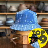 Denim Mashup Bucket Hat displayed on a wooden stand with a background of various hats on shelves, featuring a patchwork denim design and a casual style.