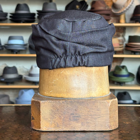 Denim Military Cap displayed on a wooden hat stand in front of shelves filled with various hats and caps in a hat shop setting.
