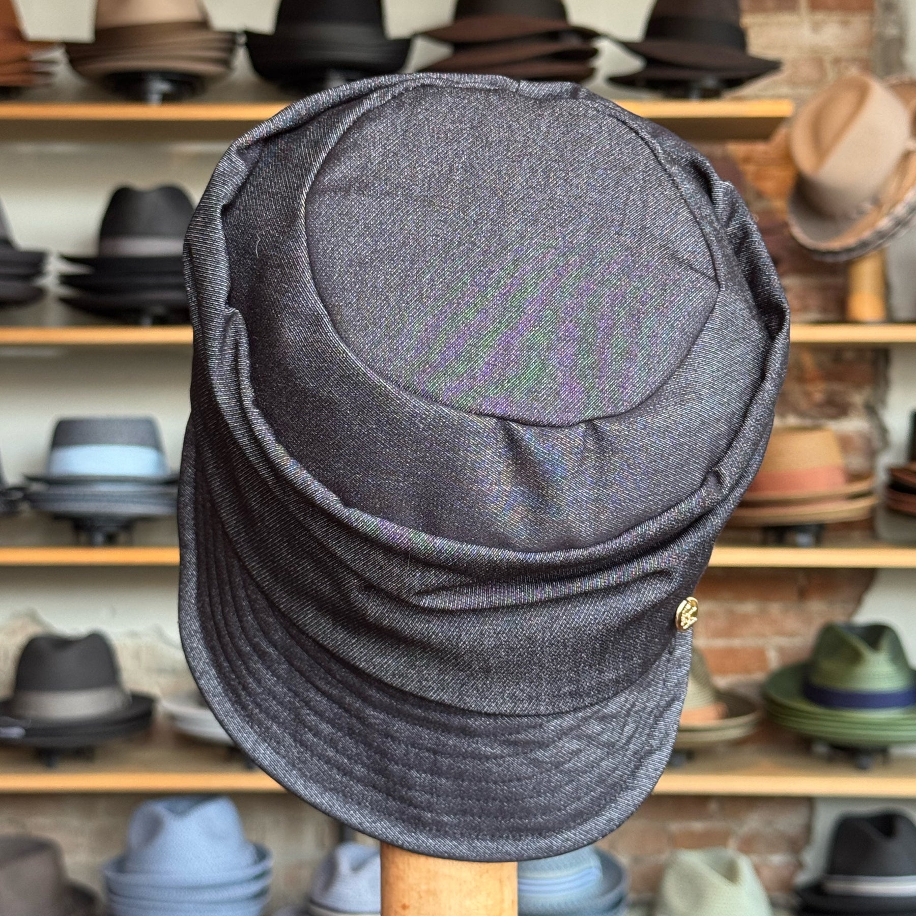 Dark denim Military Cap with soft structured crown and curved brim, displayed in a hat shop with various styles in the background.