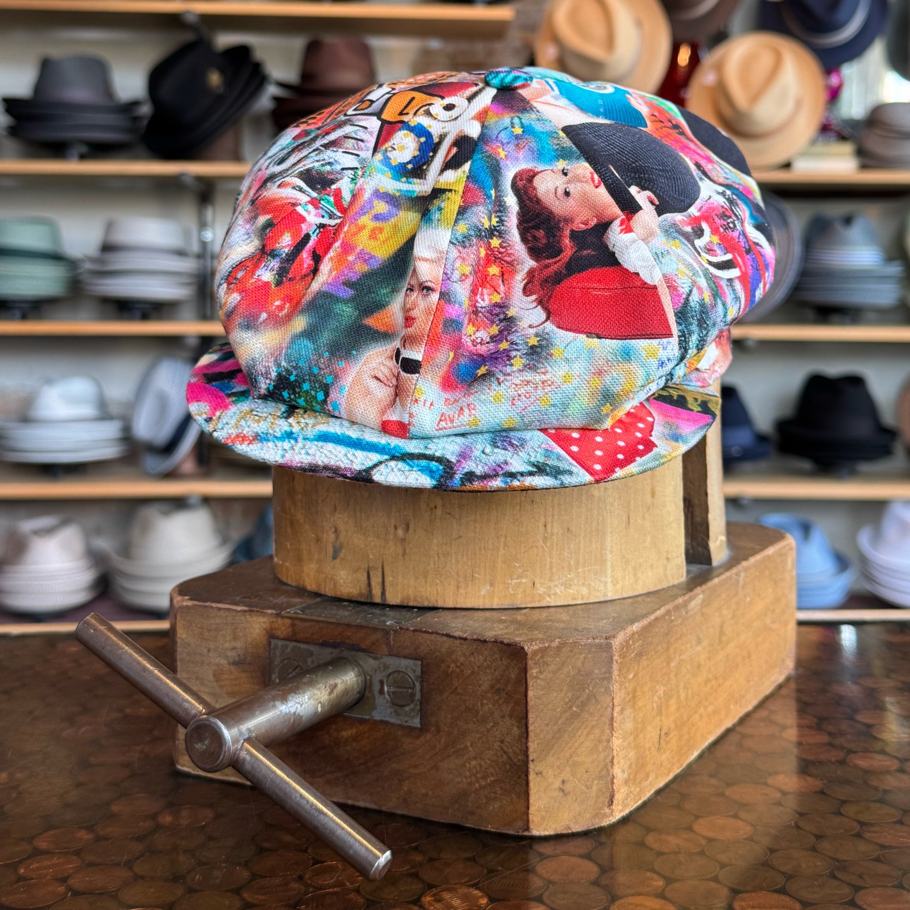 Colorful Graffiti Hatteras newsboy cap featuring vibrant urban art prints, displayed on a wooden hat blocker in a shop with various brim hats in the background.