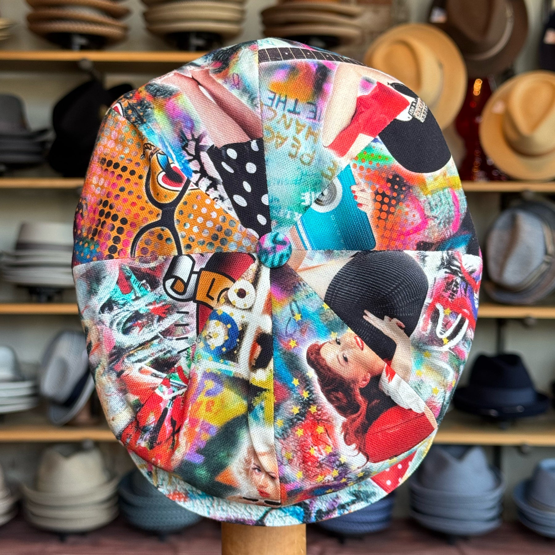 Colorful graffiti-style flat cap featuring various artistic designs and images, displayed in a hat shop, identified as Graffiti Hatteras.