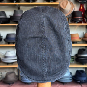 Dark pinstriped fabric Leland Two-Panel Ivy Cap displayed from the back with a softly rounded shape, set against a background of various hats on wooden shelves in a hat shop.