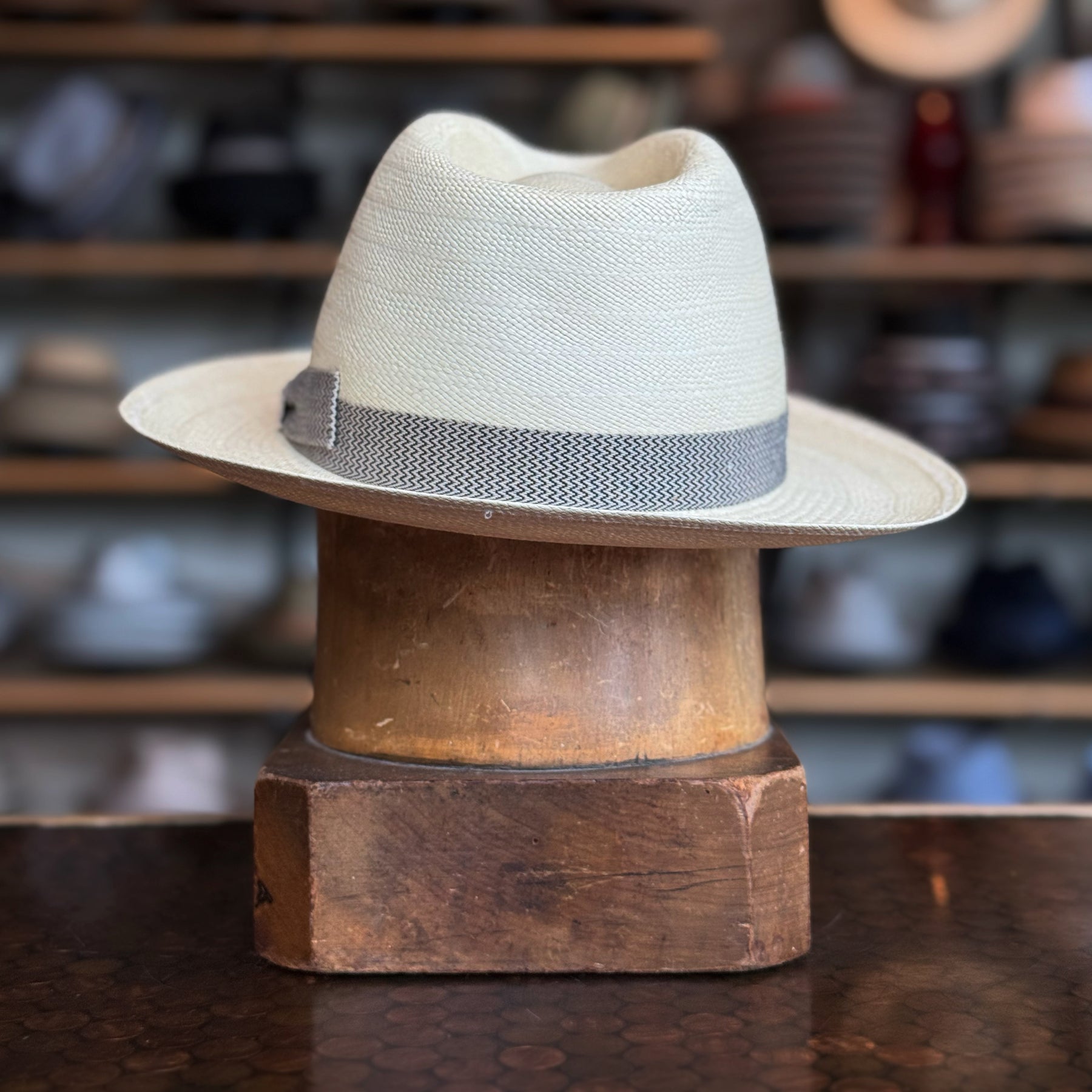 Italin Panama Fedora hat featuring a light natural woven straw design with a gray textured band, displayed on a wooden hat stand in a cozy, rustic setting.