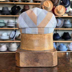 Kit Flat Cap in a soft striped fabric displayed on a wooden stand with various hats in the background in a store setting