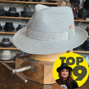 Light gray woven linen hat with a classic shape and a narrow band, displayed on a wooden stand, showcasing the Linen Maleo Fedora style.