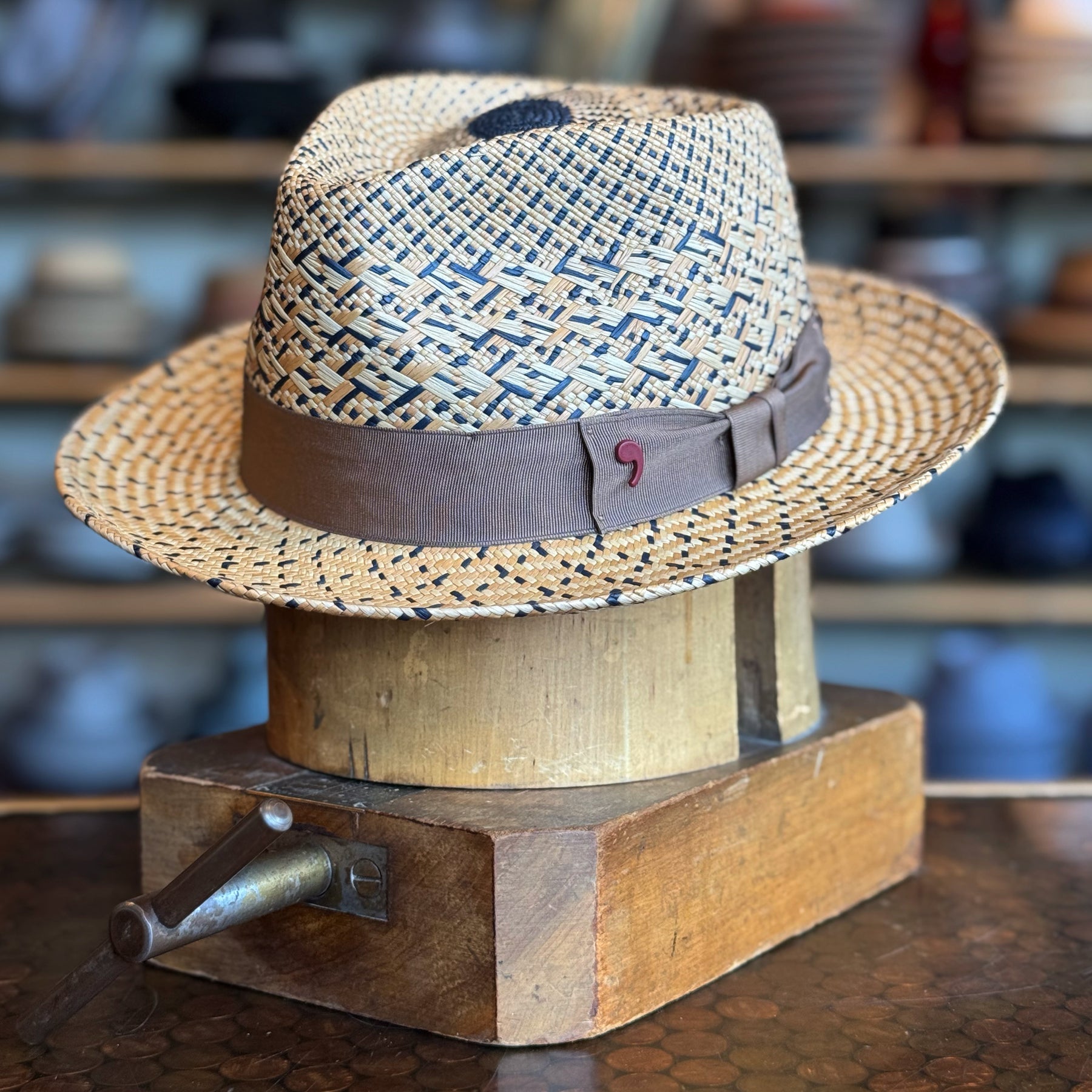 Maize Panama Fedora with a braided straw design with natural and black design and brown fabric band, displayed on a wooden hat block in a hat shop setting.