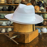 Max white brim hat displayed on a wooden hat stretcher with multiple hats in the background at a hat store.