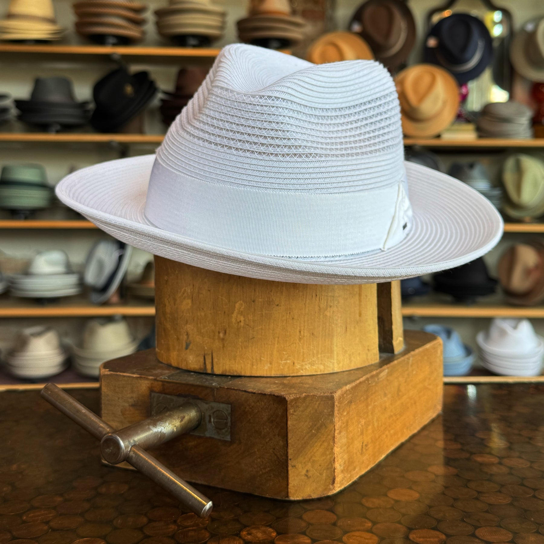 Max white brim hat displayed on a wooden hat stretcher with multiple hats in the background at a hat store.