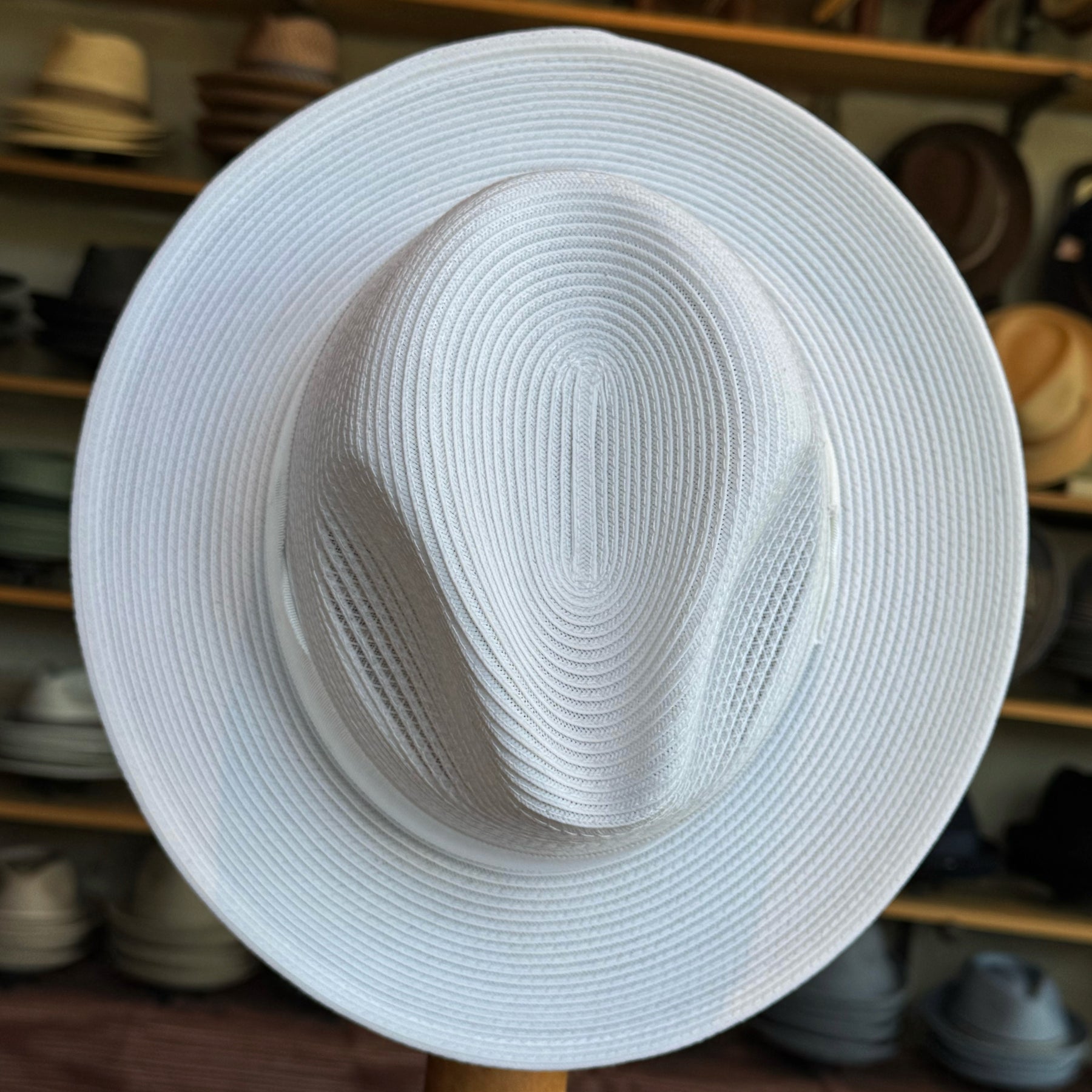 Max white wide brim hat with a structured crown, crafted from woven material, displayed in a hat shop among various other styles.