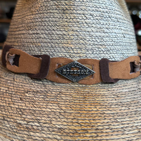 Close-up of a textured woven straw hat with a brown suede band featuring a metal Stetson logo detail, representing the Monterrey Bay style.