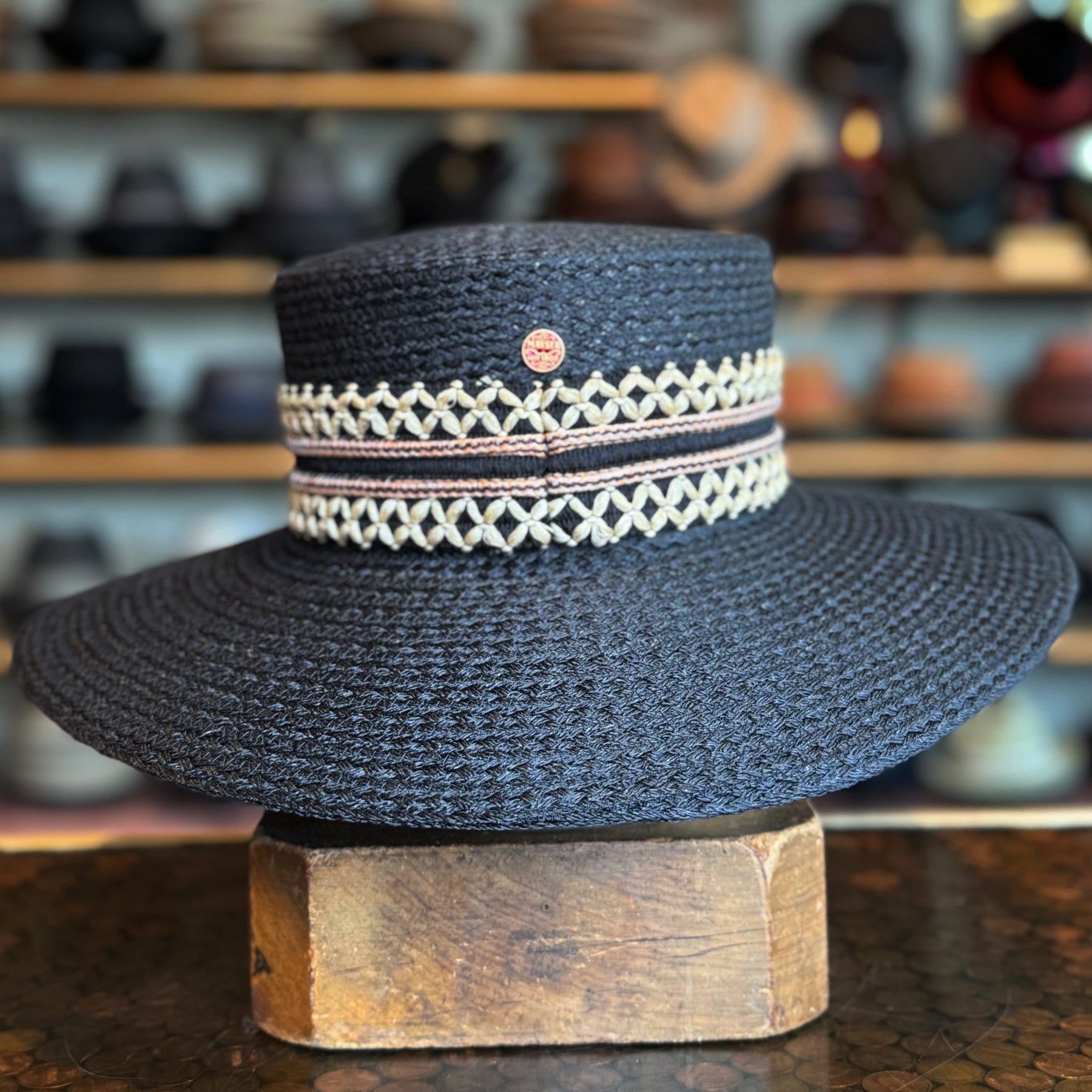 Black woven wide brim hat with decorative cream-colored and pink band detailing, featuring the design named Noreen.