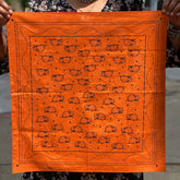 Opossum Bandana in burnt orange featuring a repeating black opossum pattern with decorative border, held by a person outdoors.