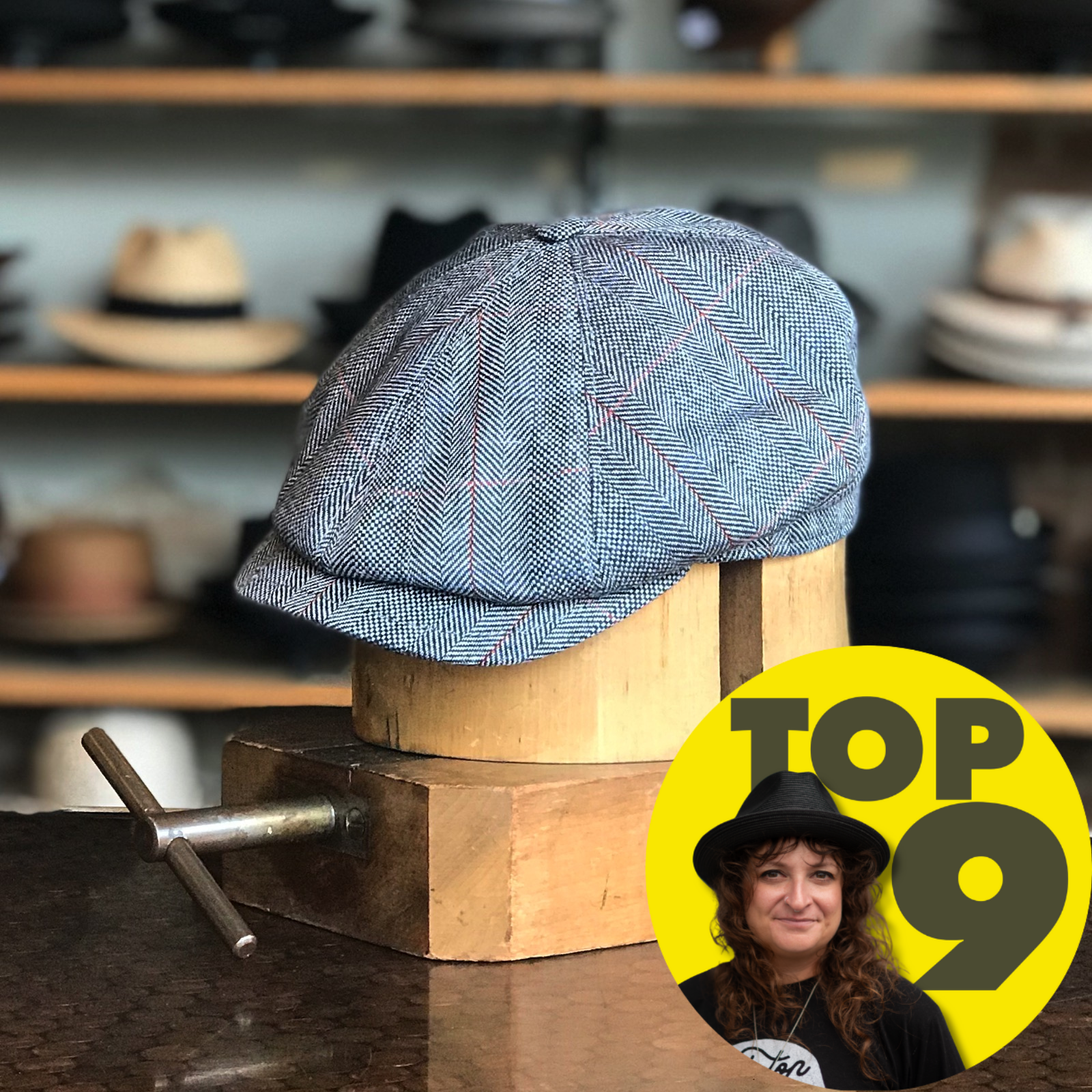 Grey herringbone patterned Palermo 6-Panel Newsboy cap displayed stylishly on a wooden hat form with blurred shelves of hats in the background.