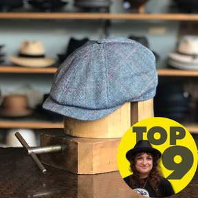 Grey herringbone patterned Palermo 6-Panel Newsboy cap displayed stylishly on a wooden hat form with blurred shelves of hats in the background.