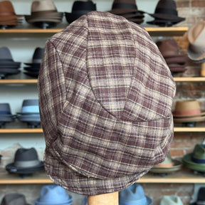 Plaid Funk Master Cap in a brown and beige checkered pattern displayed on a wooden stand with various hats in the background.