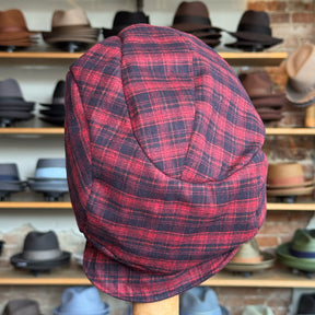 Plaid Funk Master Cap in a red and black plaid pattern displayed on a stand with shelves of various hats in the background.