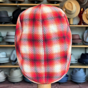 Red Check 2-Panel Ivy Cap showcasing a vibrant red plaid pattern with subtle black and white accents, displayed on a stand in front of shelves filled with various brim hats and caps.