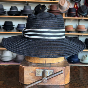 Sabine Fedora in black woven material featuring a wide brim and accented with a stylish white and black striped band, displayed on a wooden hat block.