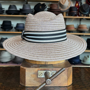 Sabine Fedora in taupe color with a wide brim and black-and-white striped band, displayed on a wooden hat block with various hats in the background.