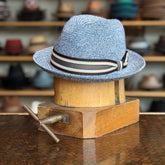 Salem hat in heather blue with a striped ribbon band, displayed on a wooden hat block, showcasing a classic brim style newsboy cap with textured weave pattern.