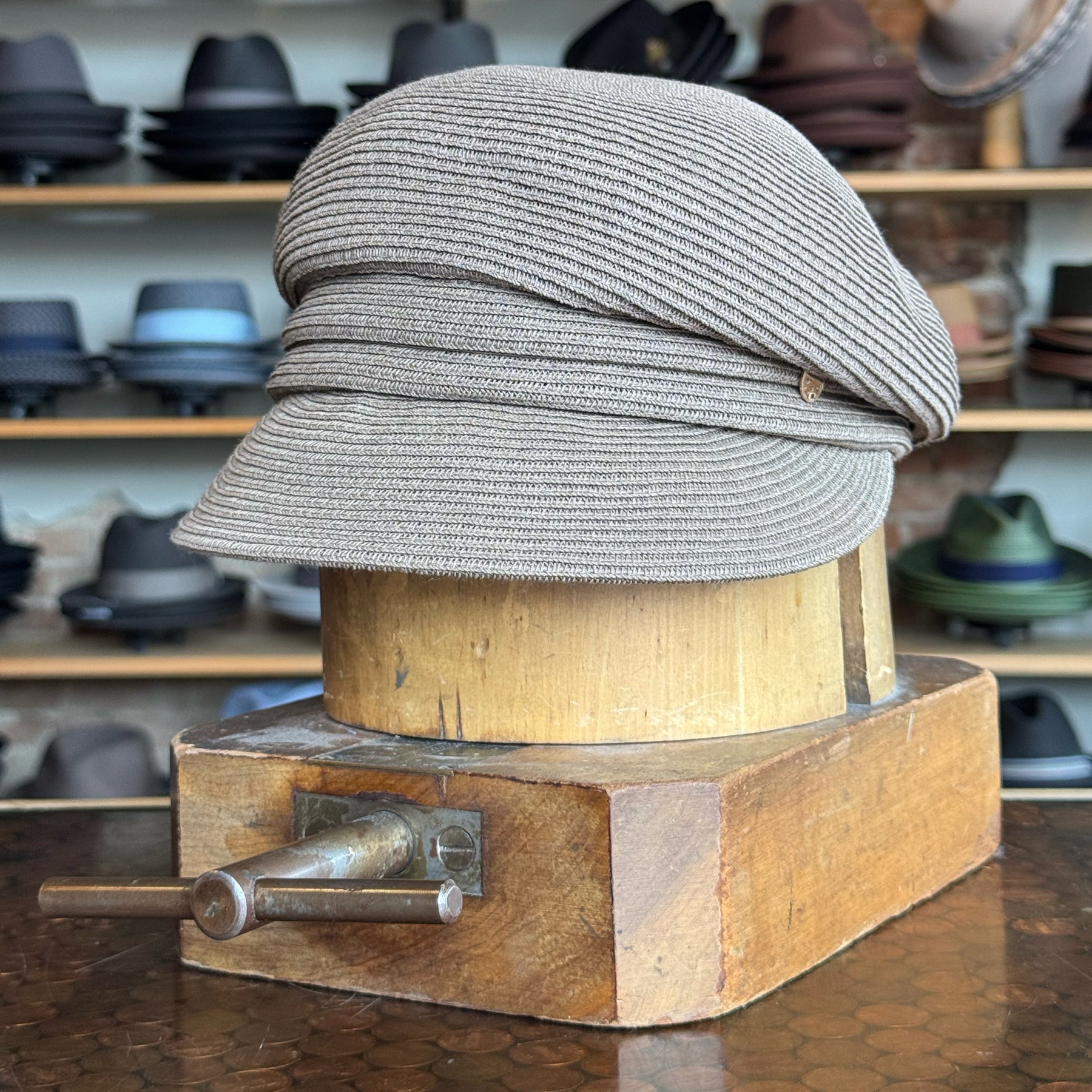 Straw Casquette in a soft milk chocolate tone displayed on a wooden hat block, surrounded by various stylish hats in the background.
