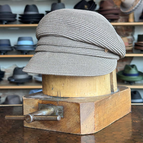 Straw Casquette in a soft milk chocolate tone displayed on a wooden hat block, surrounded by various stylish hats in the background.