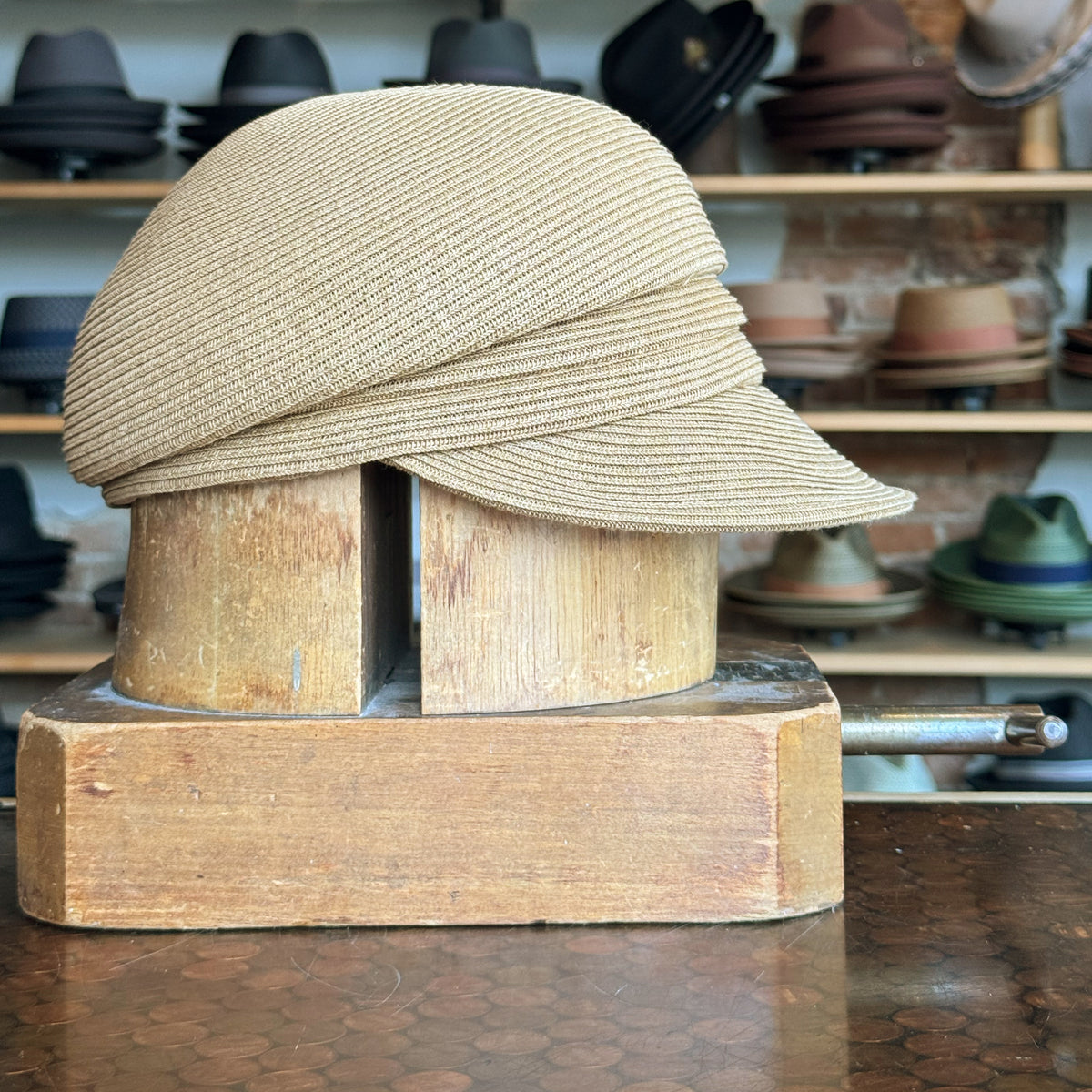 Straw Casquette with a soft woven texture displayed on a wooden hat block, surrounded by various hats in the background, showcasing a stylish and casual design.