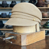 Straw Casquette displayed on a wooden hat block, featuring a woven natural straw texture with a soft, structured design and a small metallic accent on the side.