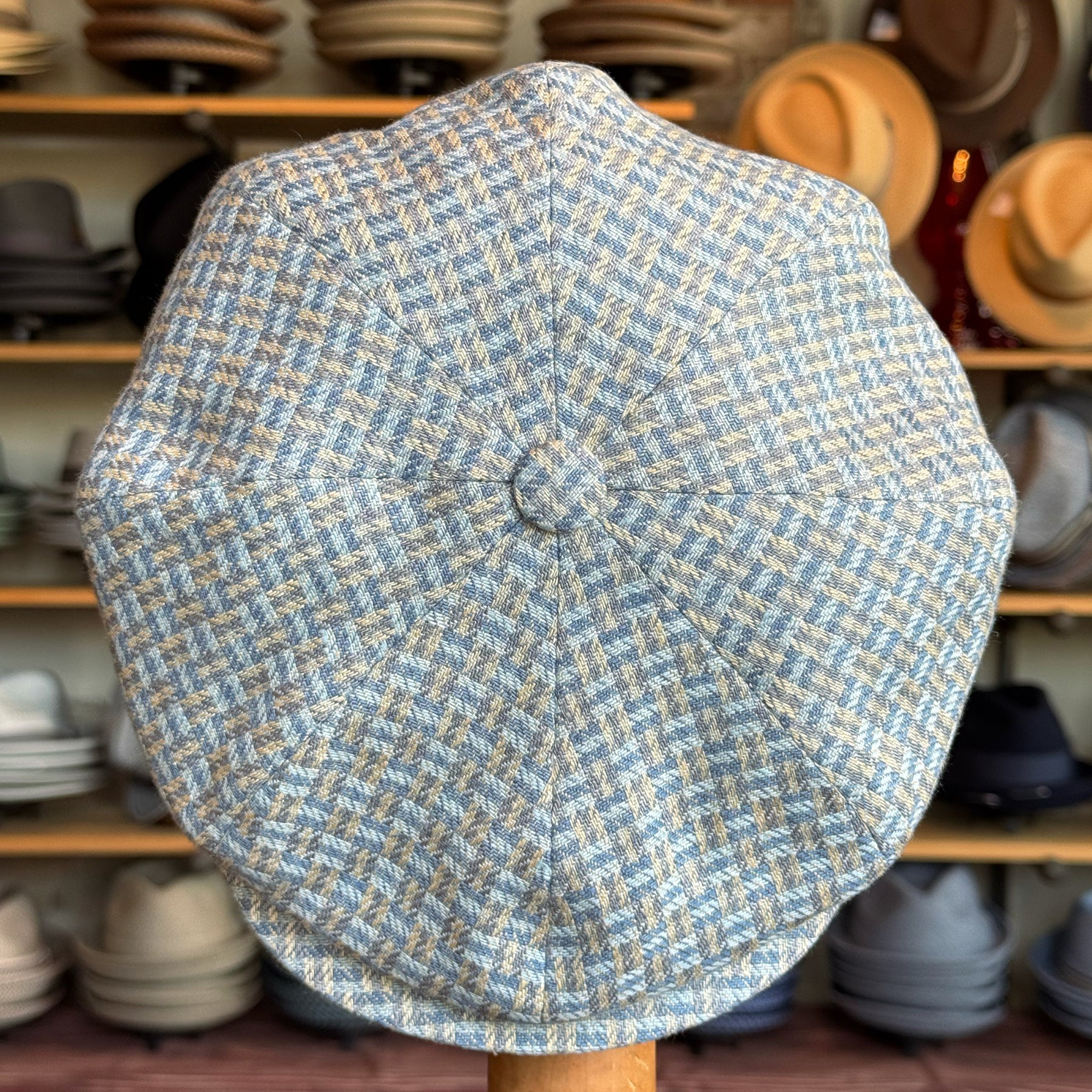 Tetris Jacquard Newsboy cap in a textured blue and beige woven pattern displayed on a stand with shelves of various hats in the background