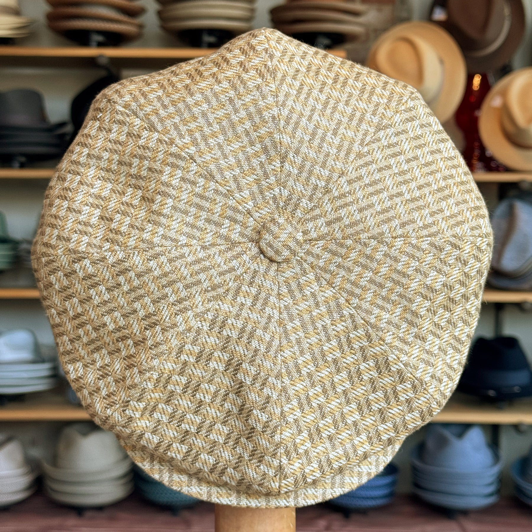 Tetris Jacquard Newsboy cap featuring a textured woven pattern in beige and light brown tones, displayed in a hat shop with various other hats in the background.