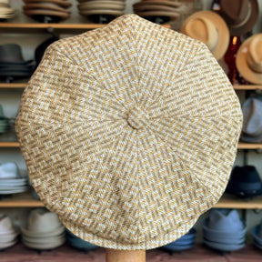 Tetris Jacquard Newsboy cap featuring a textured woven pattern in beige and light brown tones, displayed in a hat shop with various other hats in the background.