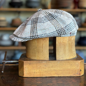 Light beige and brown plaid newsboy cap displayed on a wooden hat block, showcasing the classic style and texture of the Textured Linen Hatteras hat.