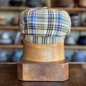 The Brightest Hatteras newsboy cap displayed on a wooden hat block, featuring a colorful plaid pattern with shades of blue, green, and beige, showcasing classic brim hat style.