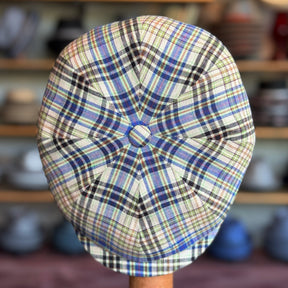 The Brightest Hatteras plaid newsboy cap with blue, green, and cream tones on a wooden hat stand in a cozy shop setting.