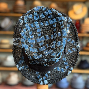 The Denim Top Hat displayed in a woven pattern of blue and black denim material, showcasing a classic top hat shape with a slightly textured fabric and a black band around the base.