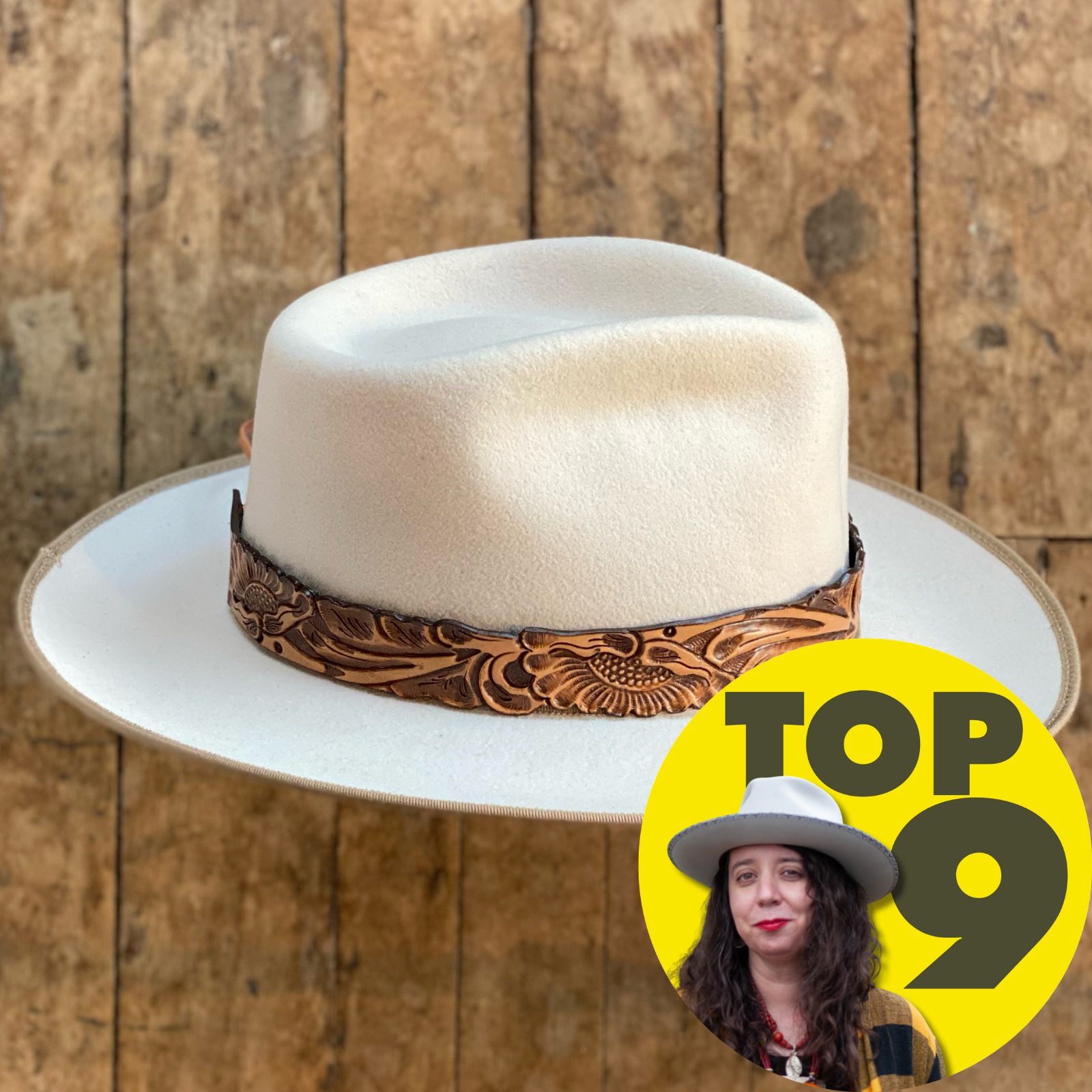 Cream-colored wide brim hat featuring a detailed Tooled Leather Hat Band with floral patterns, resting on a rustic wooden surface.
