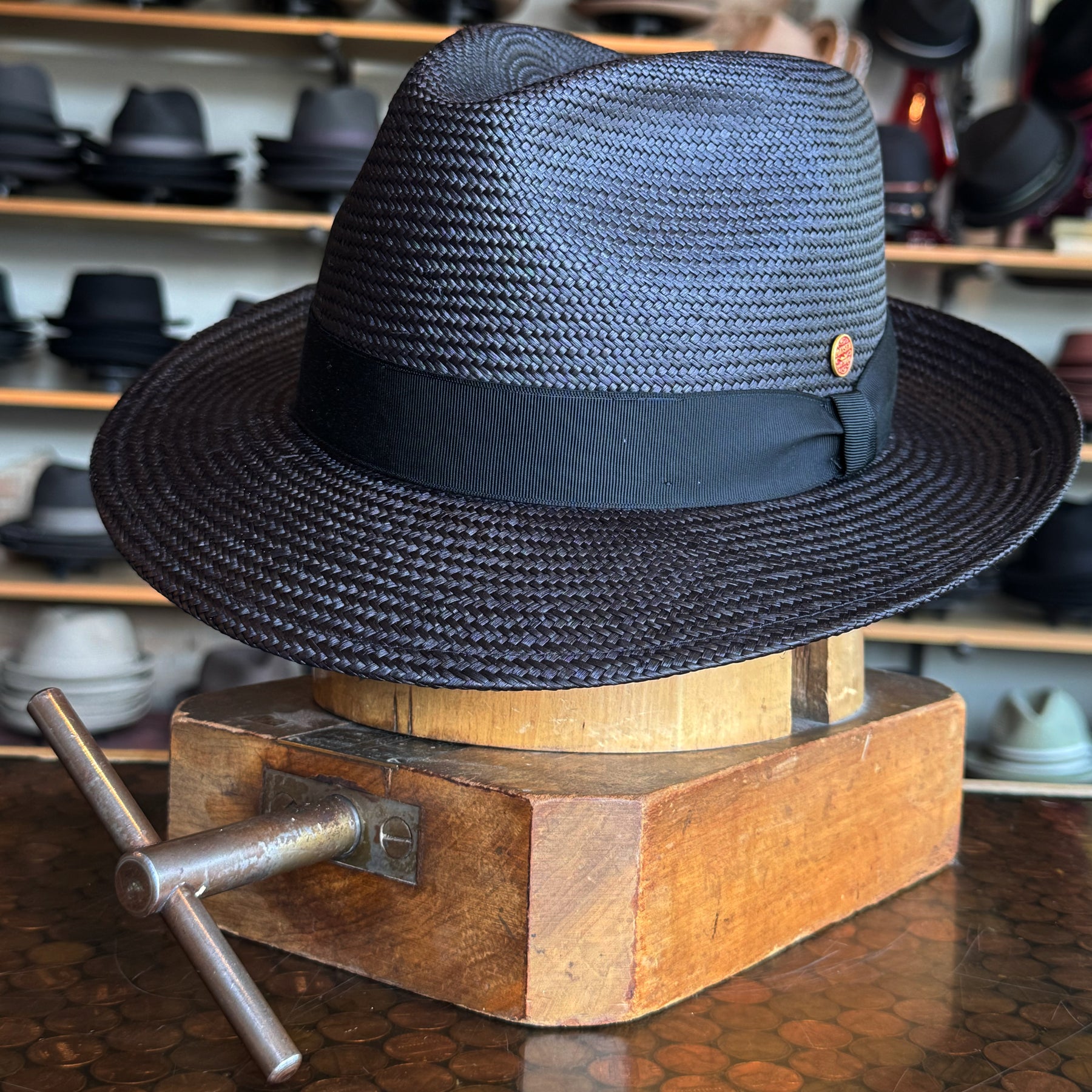 Torino black woven fedora hat with a wide brim and black band displayed on a wooden hat block with other hats in the background