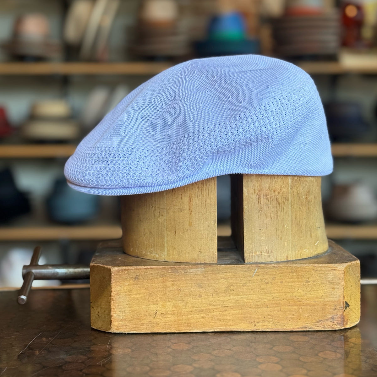Light blue Tropic 504 Ventair flat cap displayed on a wooden hat block with a textured knit design and a soft brim.