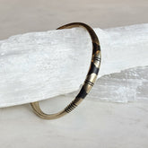 Tuareg Coin Silver Bracelet J featuring intricate dark and silver geometric patterns on a slender cuff resting on a textured white crystal background.